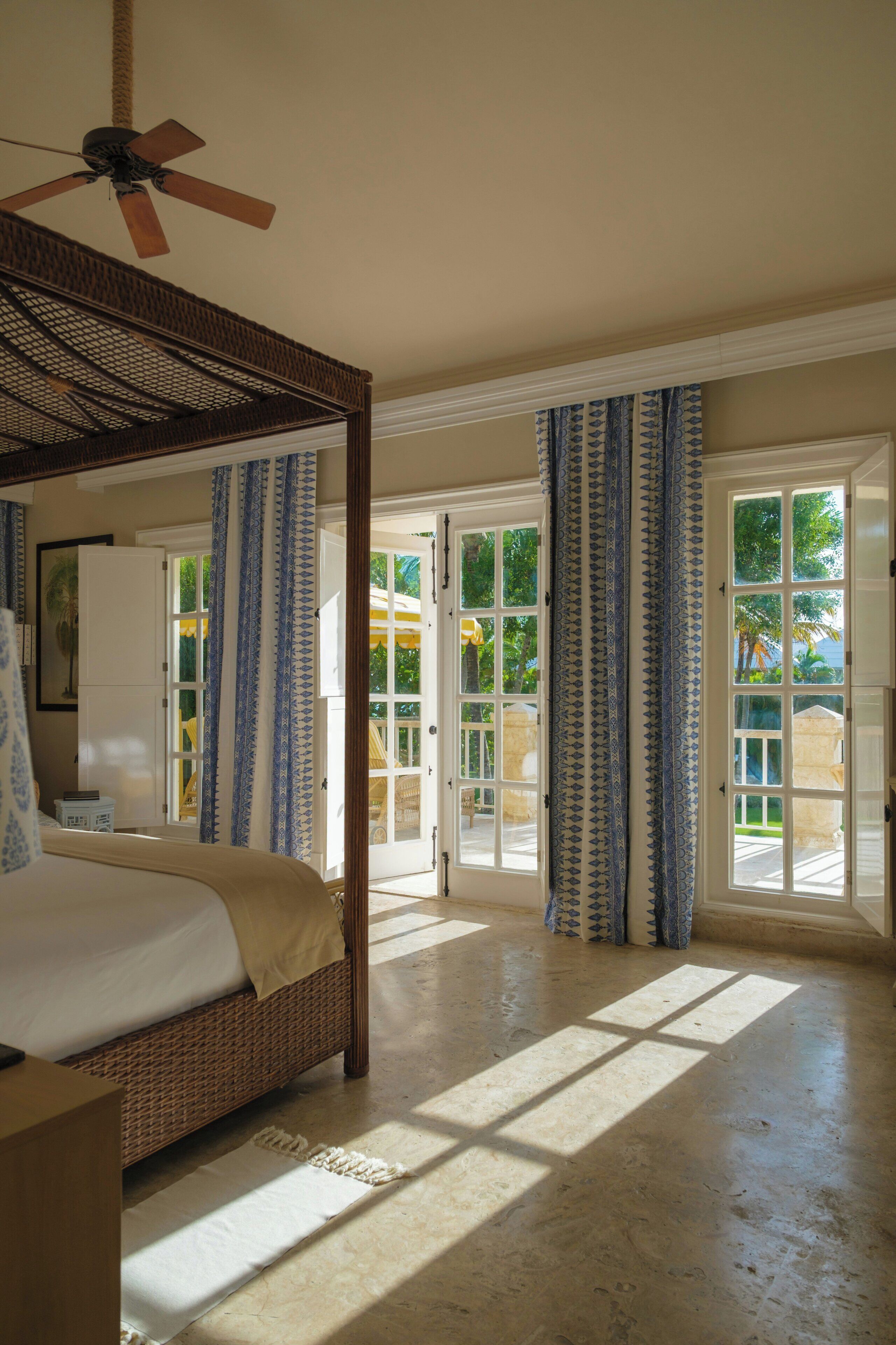 A bedroom with a four-poster bed, a ceiling fan, and a view through a glass door to an outdoor area.