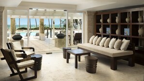 A modern lounge area with a sofa, chairs, and a coffee table, overlooking a pool and beach. - Tortuga Bay Hotel (Punta Cana)