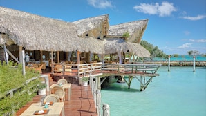 An overwater bungalows with thatched roofs, wooden deck, and dining area overlooking turquoise waters. - Tortuga Bay Hotel (Punta Cana)