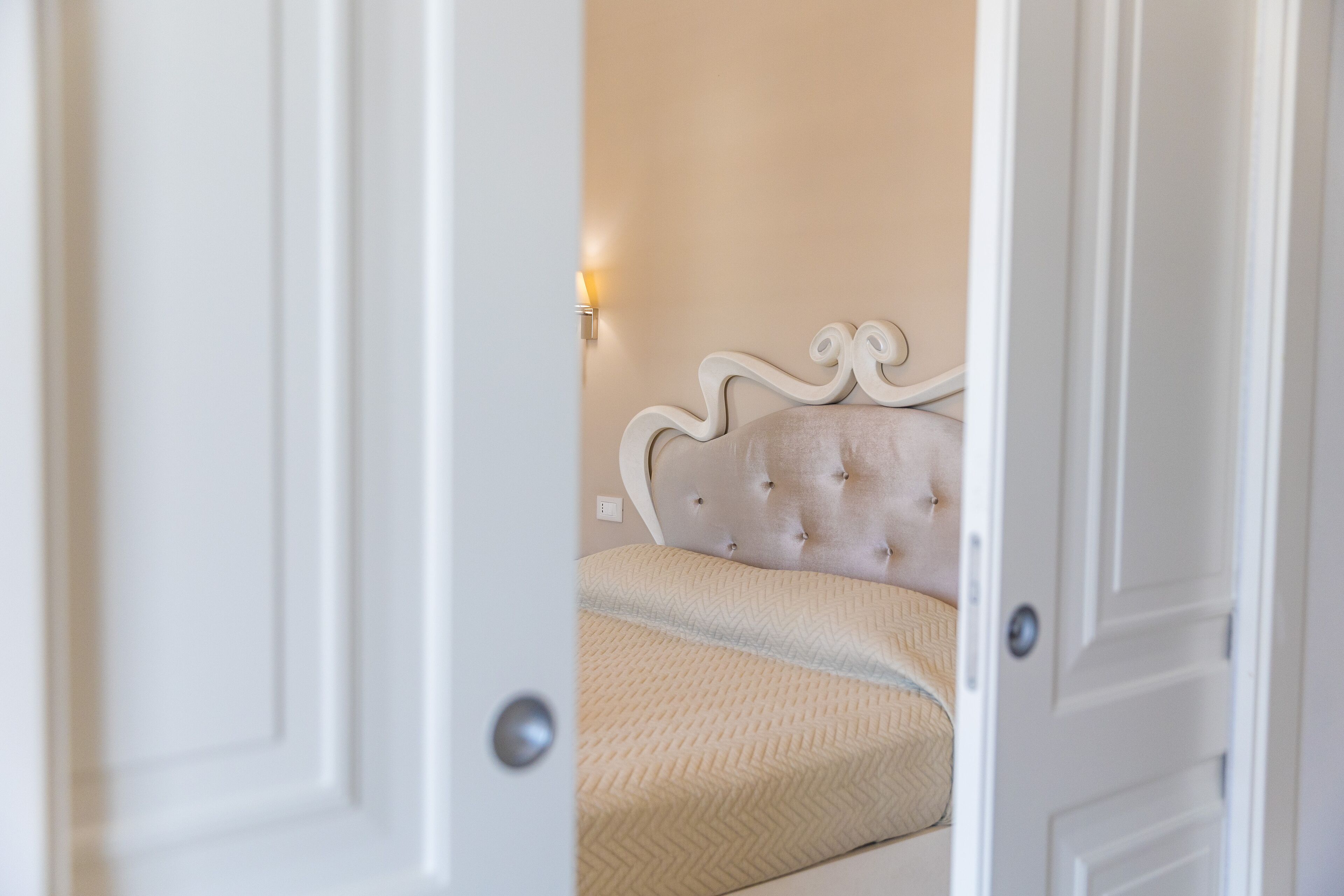 A bedroom with a tufted headboard, a bed with a textured bedspread, and a wall-mounted light fixture.