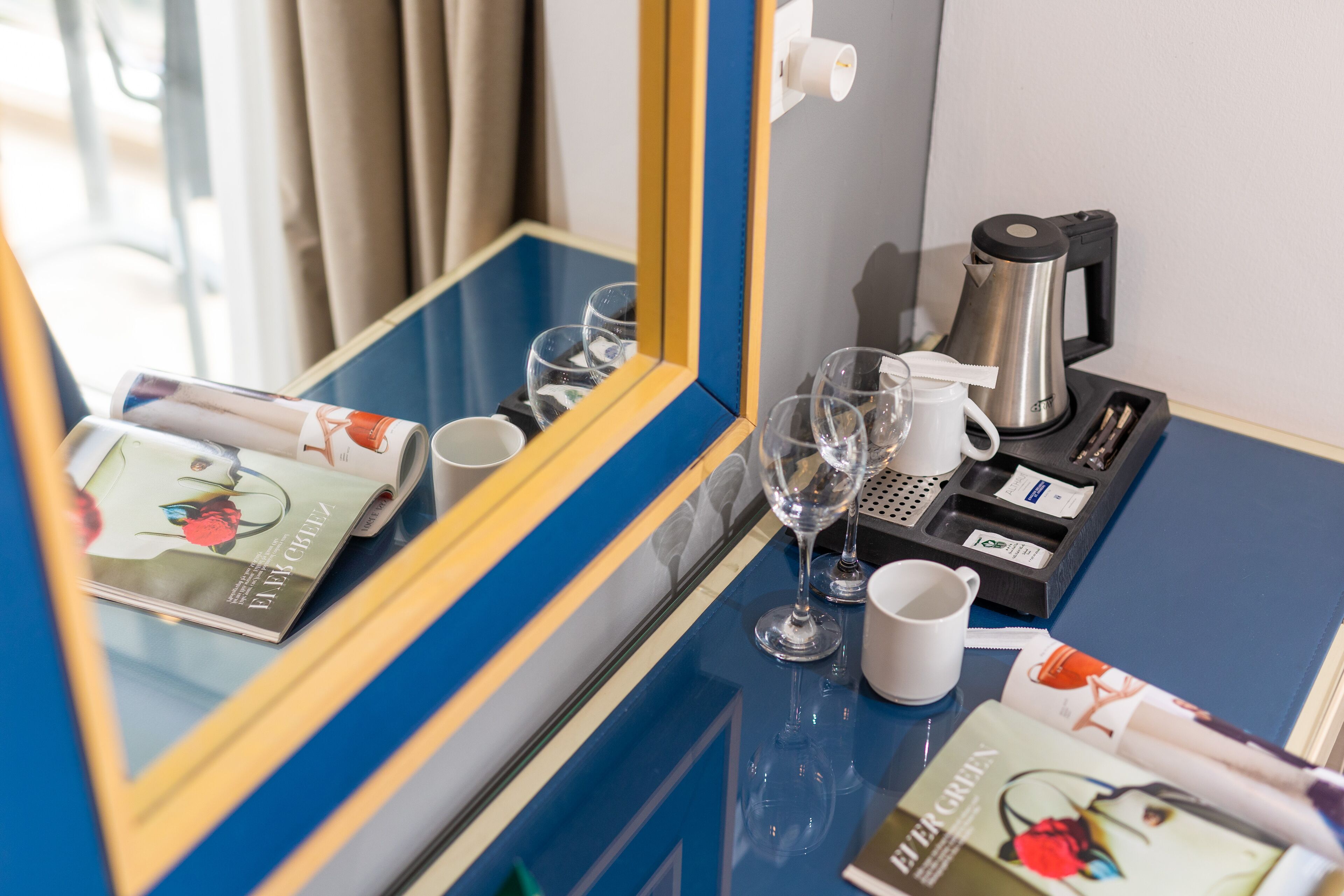 Quarto de hotel com minibar azul e amarelo, máquina de café e uma revista no balcão.