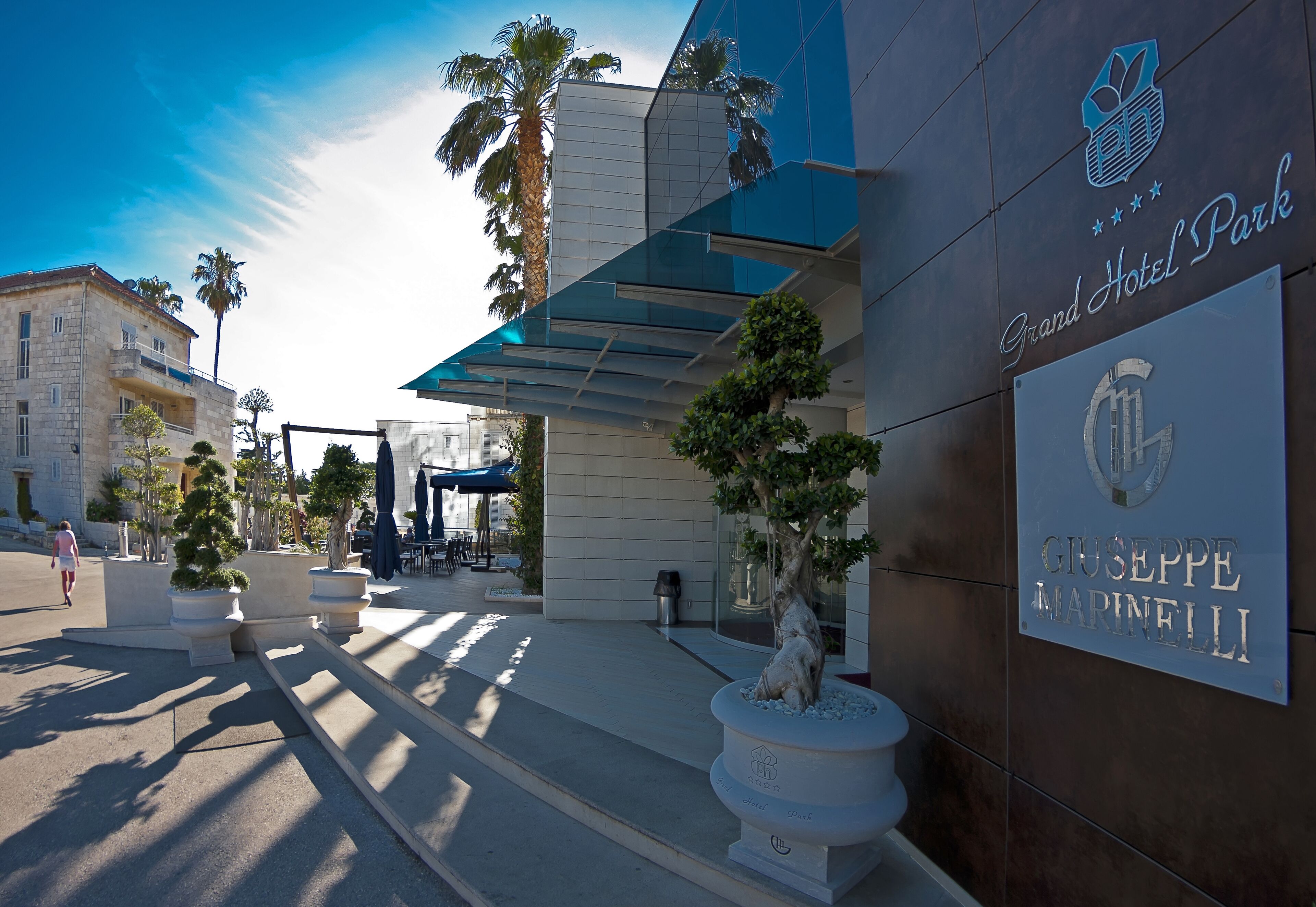 The Grand Hotel Park entrance with a modern facade, a bronze plaque, and a palm tree.