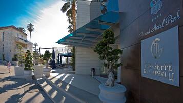 The Grand Hotel Park entrance with a modern facade, a bronze plaque, and a palm tree.