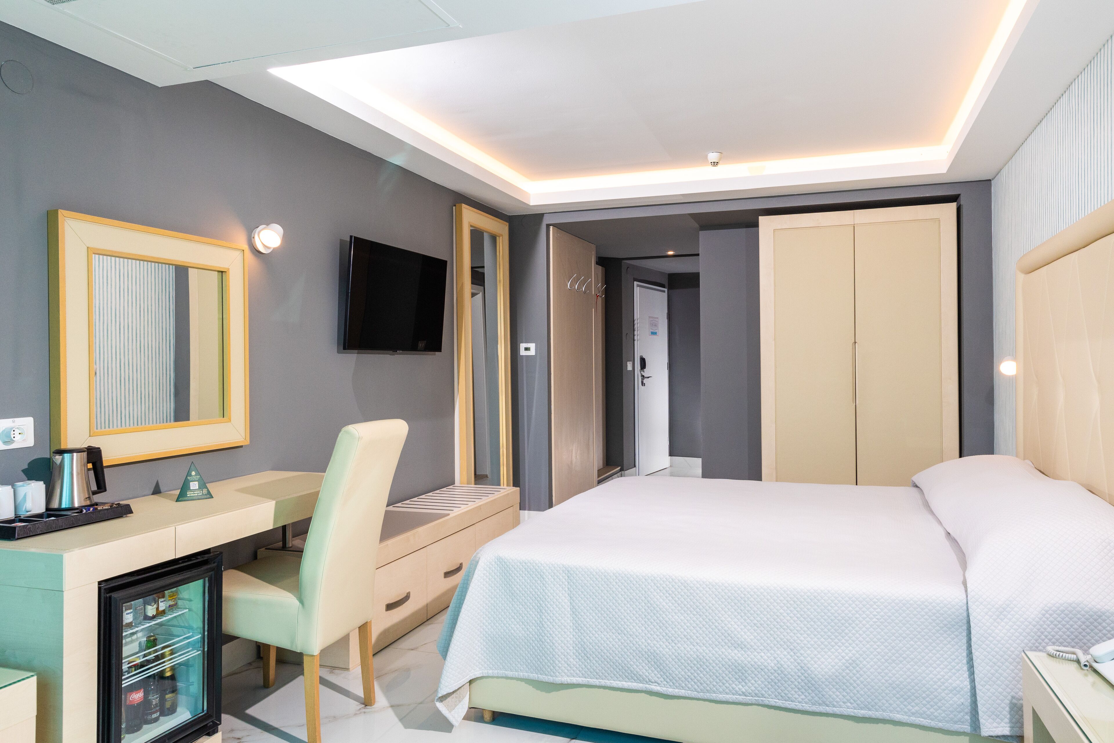 Une chambre d’hôtel moderne équipée d’un lit, d’un bureau avec un ordinateur, d’une chaise, d’une télévision et d’une armoire.