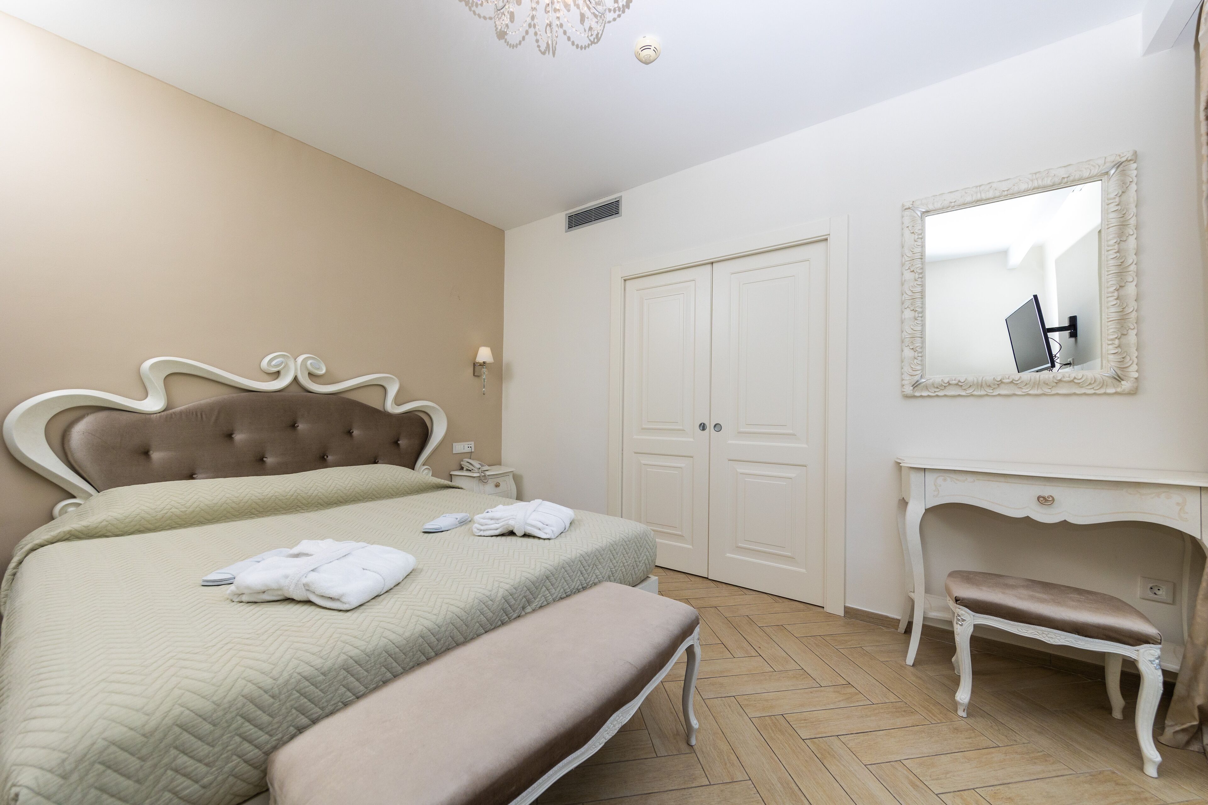 A bedroom with a bed, bedside table, bench, wardrobe, and a mirror.