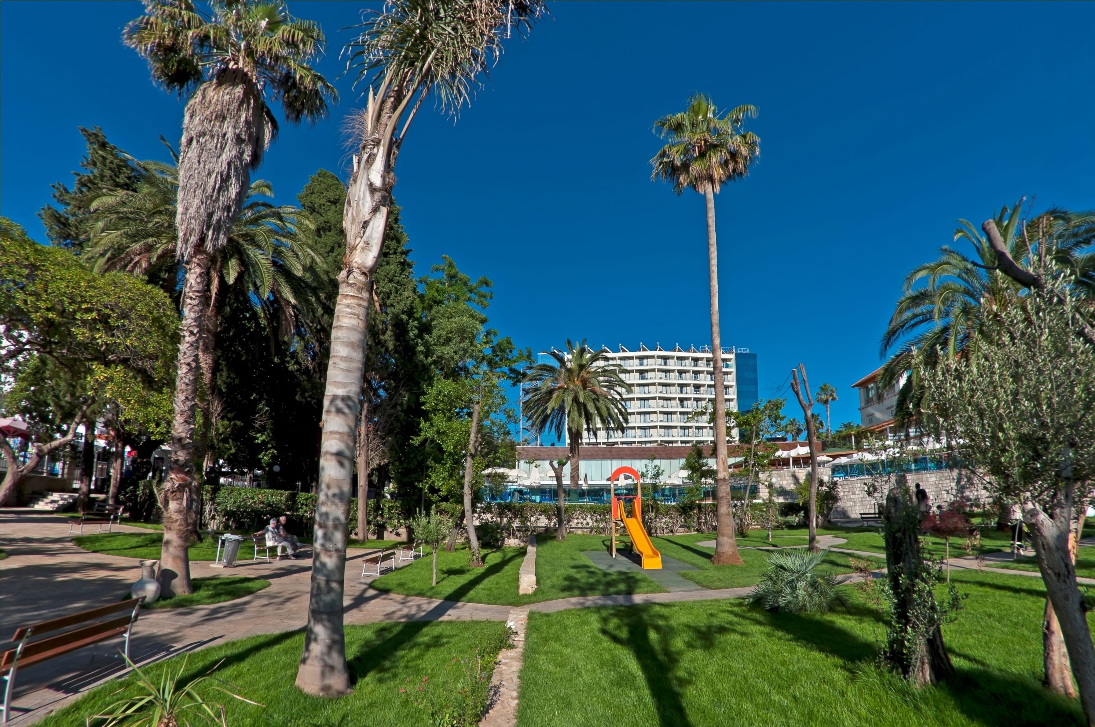 Ein Park mit Palmen, einem Spielplatz und einem Gebäude im Hintergrund.