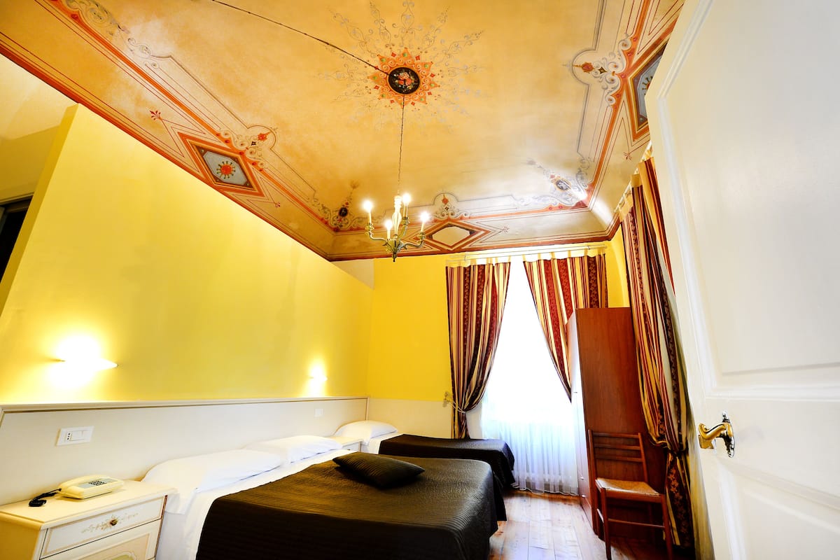 A hotel room with two beds, a chandelier, and a wooden chair.