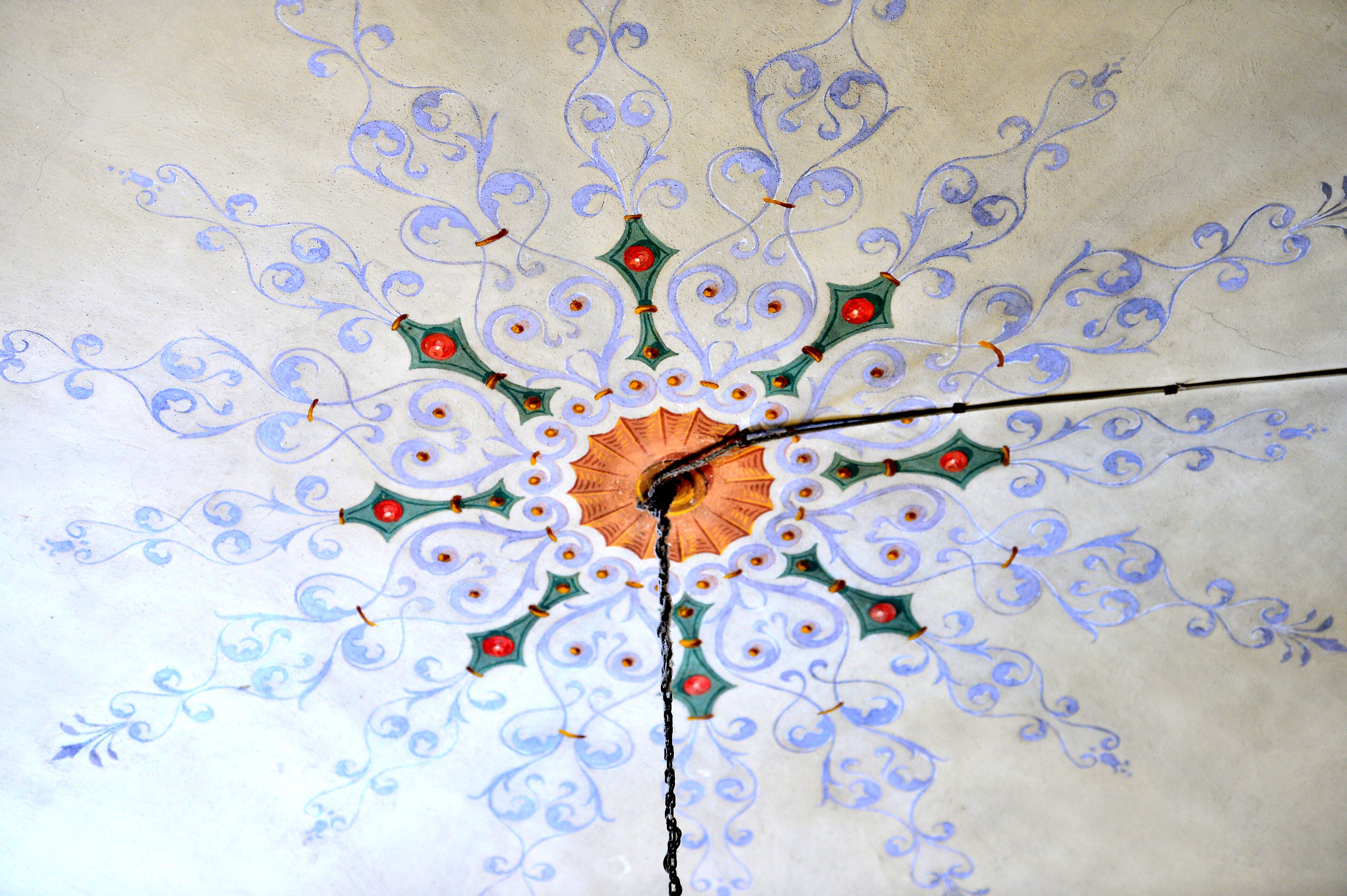 Un plafond orné d’un motif géométrique, avec un dessin central orange entouré d’éléments bleus et verts.