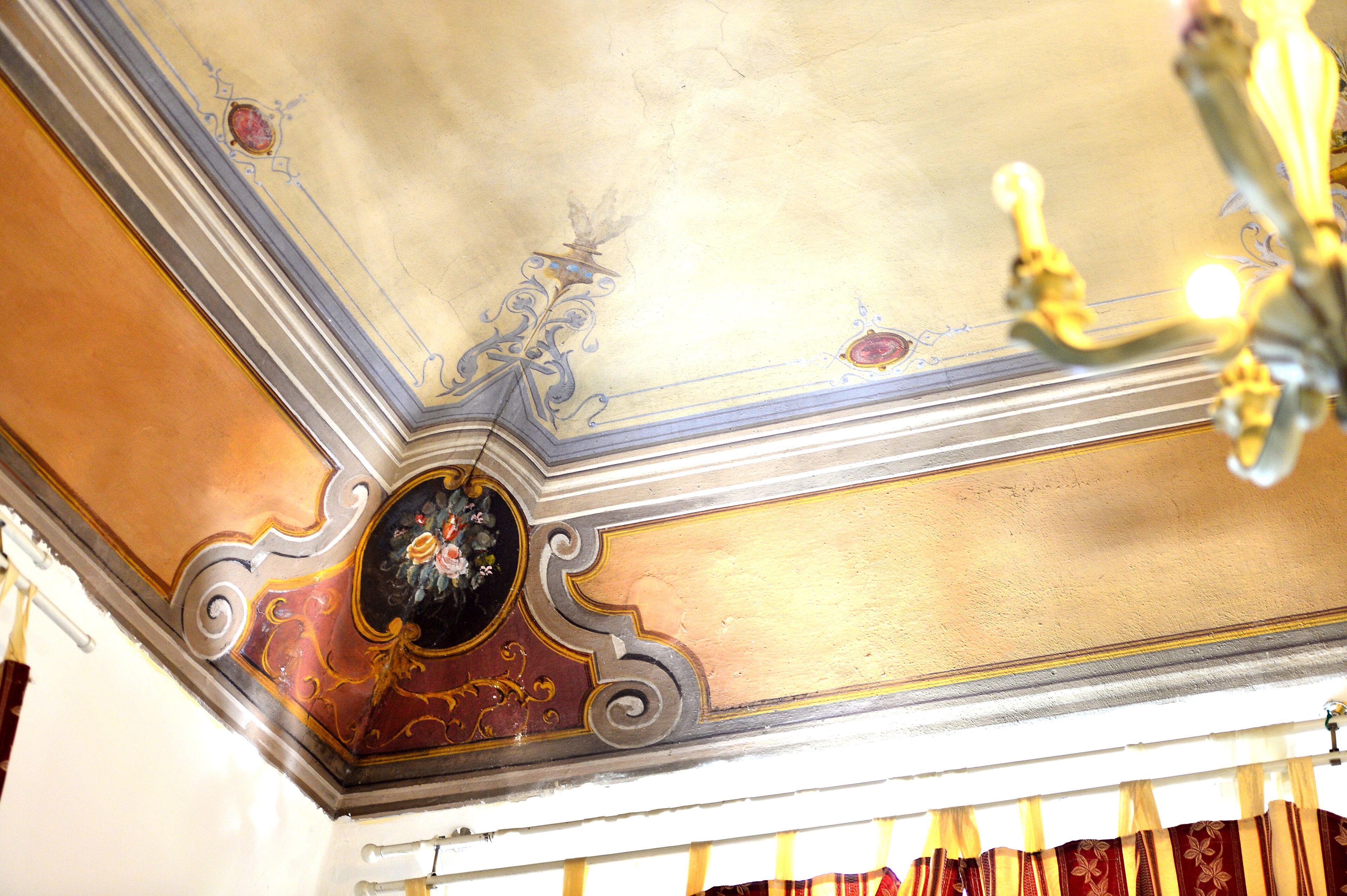 Un soffitto con decorazioni elaborate in oro e bianco, un lampadario e un quadro incorniciato.