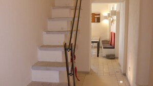 A staircase with a handrail leading to a landing. The landing opens into a hallway with a tiled floor and a door leading to a room with a bed and a nightstand. - Micalò ArtRooms (Naples)