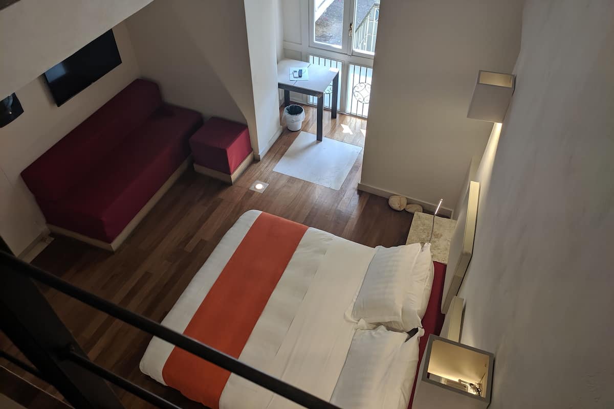 A room with a bed, a red sofa, a small table, and a window.
