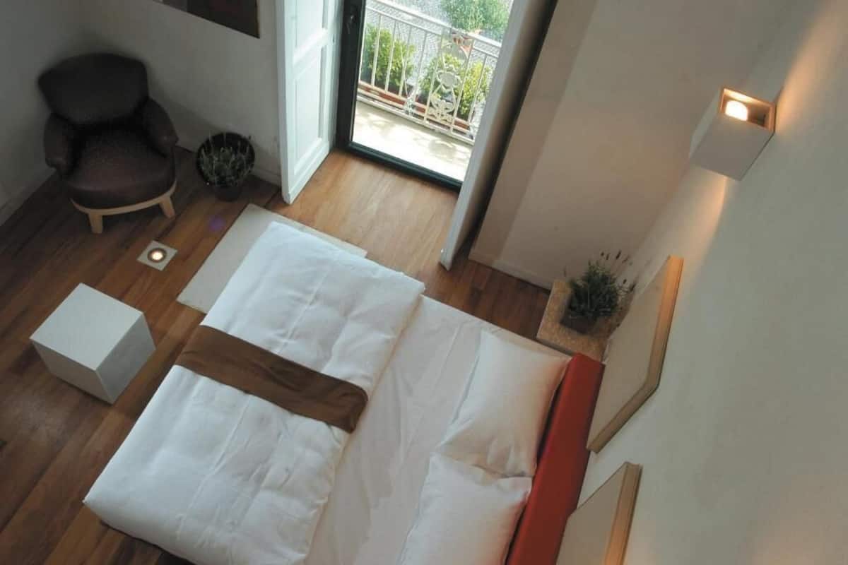 A bedroom with a bed, a chair, a small table, and a potted plant.