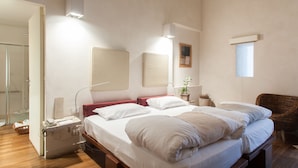 A bedroom with a large bed, bedside tables, a wicker chair, and a small window. - Micalò ArtRooms (Naples)