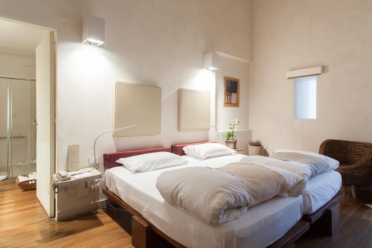 A bedroom with a large bed, bedside tables, a wicker chair, and a small window.