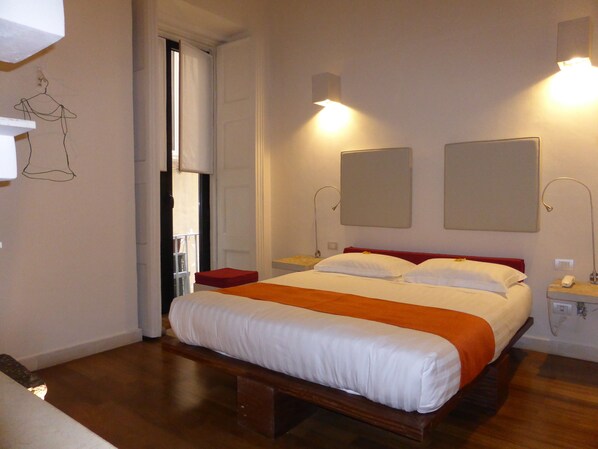 Habitación de hotel ordenada con una cama grande, mesitas de noche y una puerta que da a un balcón.