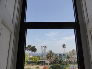 A view through a window with a clear sky, palm trees, and a distant view of the sea. - Micalò ArtRooms (Naples)