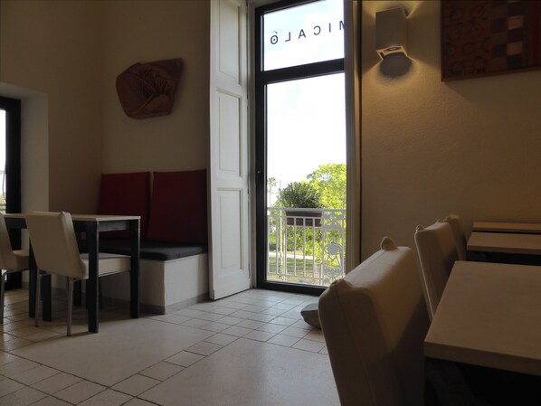 A cafe with a seating area featuring tables and chairs, a large window with a view of greenery, and a wall-mounted artwork.