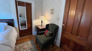 Une chambre à coucher avec un lit, une chaise, une table de chevet, une lampe, une porte et un miroir.