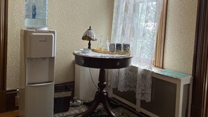 Une pièce équipée d’un distributeur d’eau, d’une table avec une lampe et d’une fenêtre ornée de rideaux en dentelle.