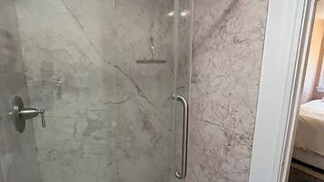 Une douche fermée par des parois de verre, dotée d’un pommeau de douche à main, d’une porte en verre et d’une poignée en métal.