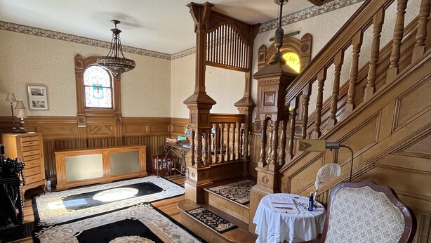 Une pièce spacieuse avec un escalier en bois, une grande fenêtre ornée de vitraux et un tapis à motifs sur le sol.