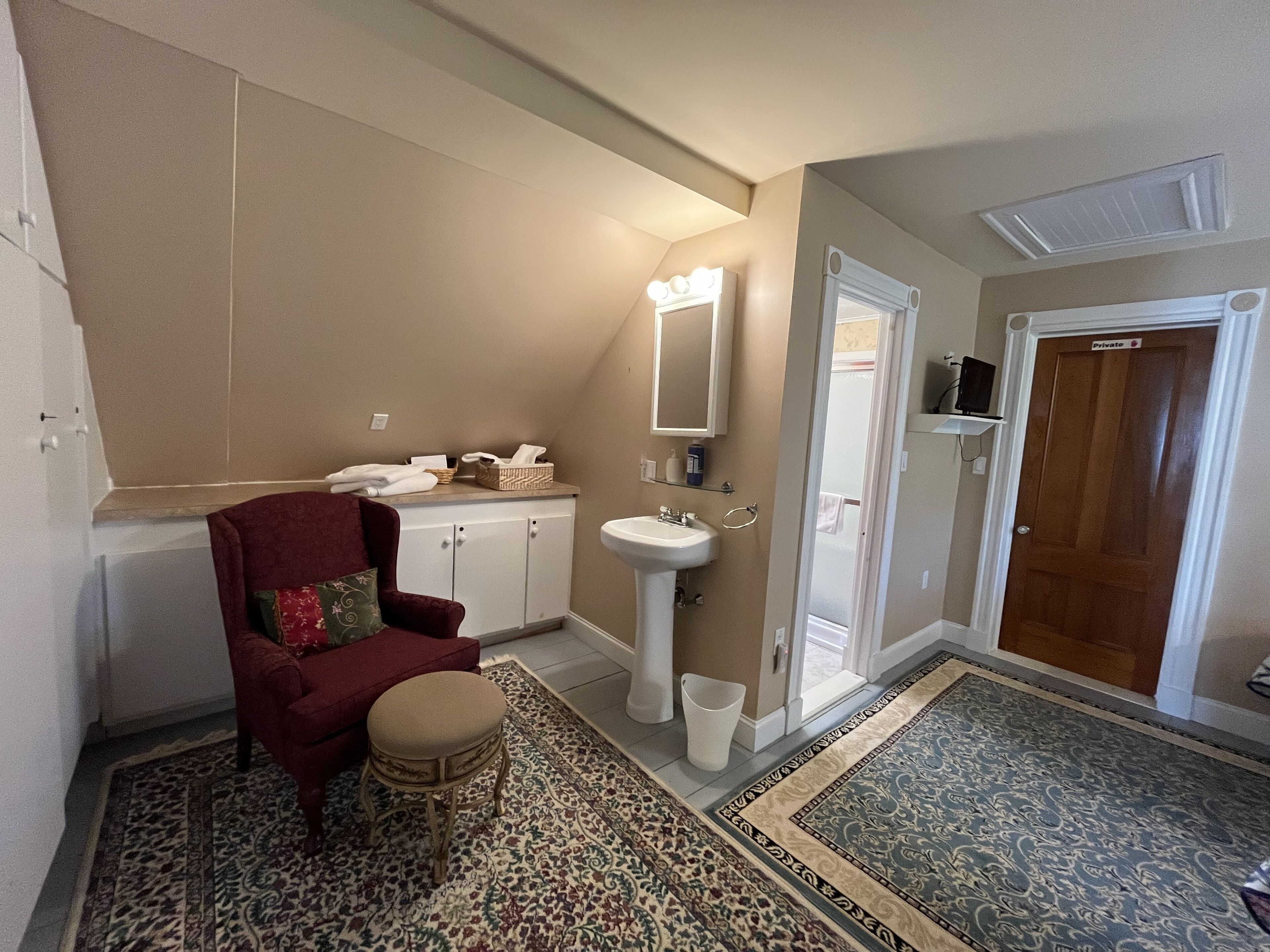 A bathroom with a vanity, sink, mirror, and a red chair.