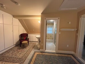 A hallway with a patterned carpet, a red chair, a white closet, and a door leading to a bathroom. - Cheney House B&B (Ashland)