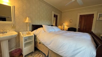 Ein Hotelzimmer mit einem Bett, einem Nachttisch mit Lampe, einem Spiegel, einem Deckenventilator und einer Tür.