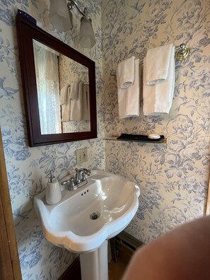 Un baño con lavamanos blanco, un espejo y papel tapiz con motivos florales.