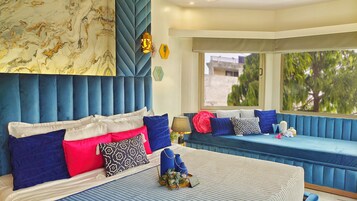 A modern bedroom with a large bed, a sofa bed, and a view of greenery outside.