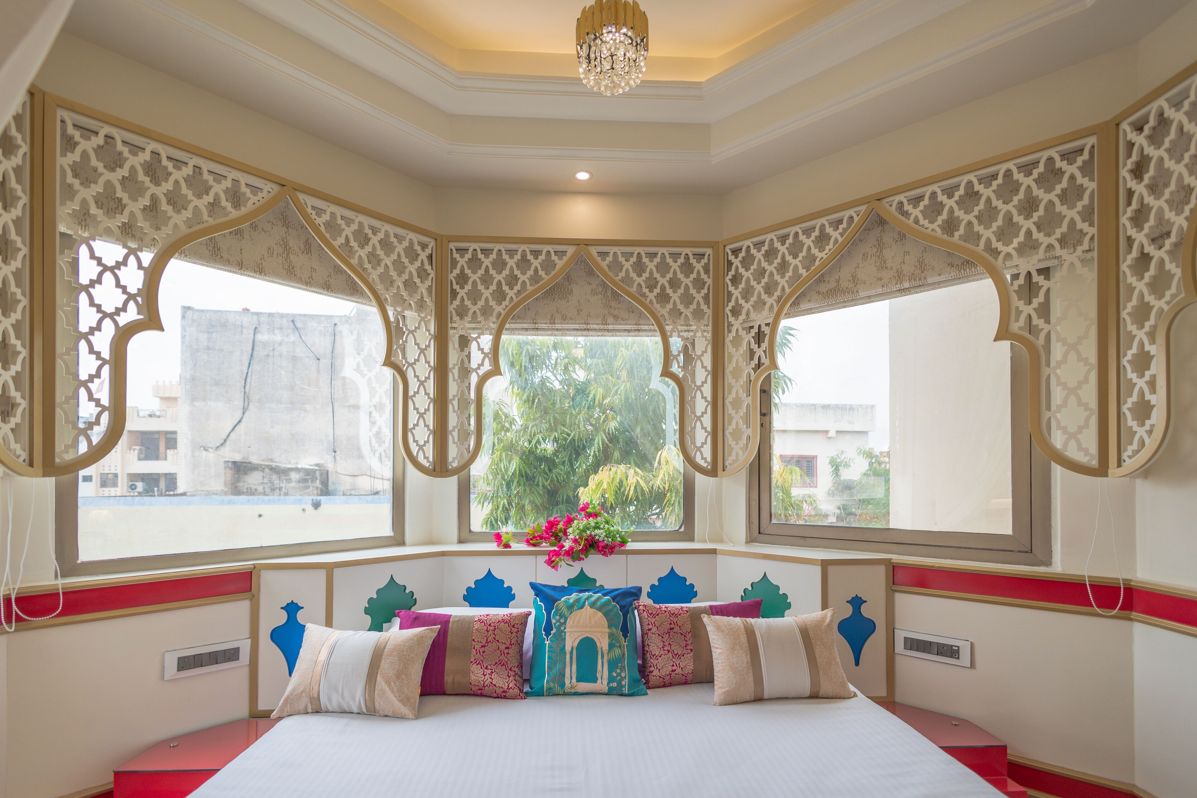 A room with a bed, decorative pillows, a window with a view, and a chandelier.