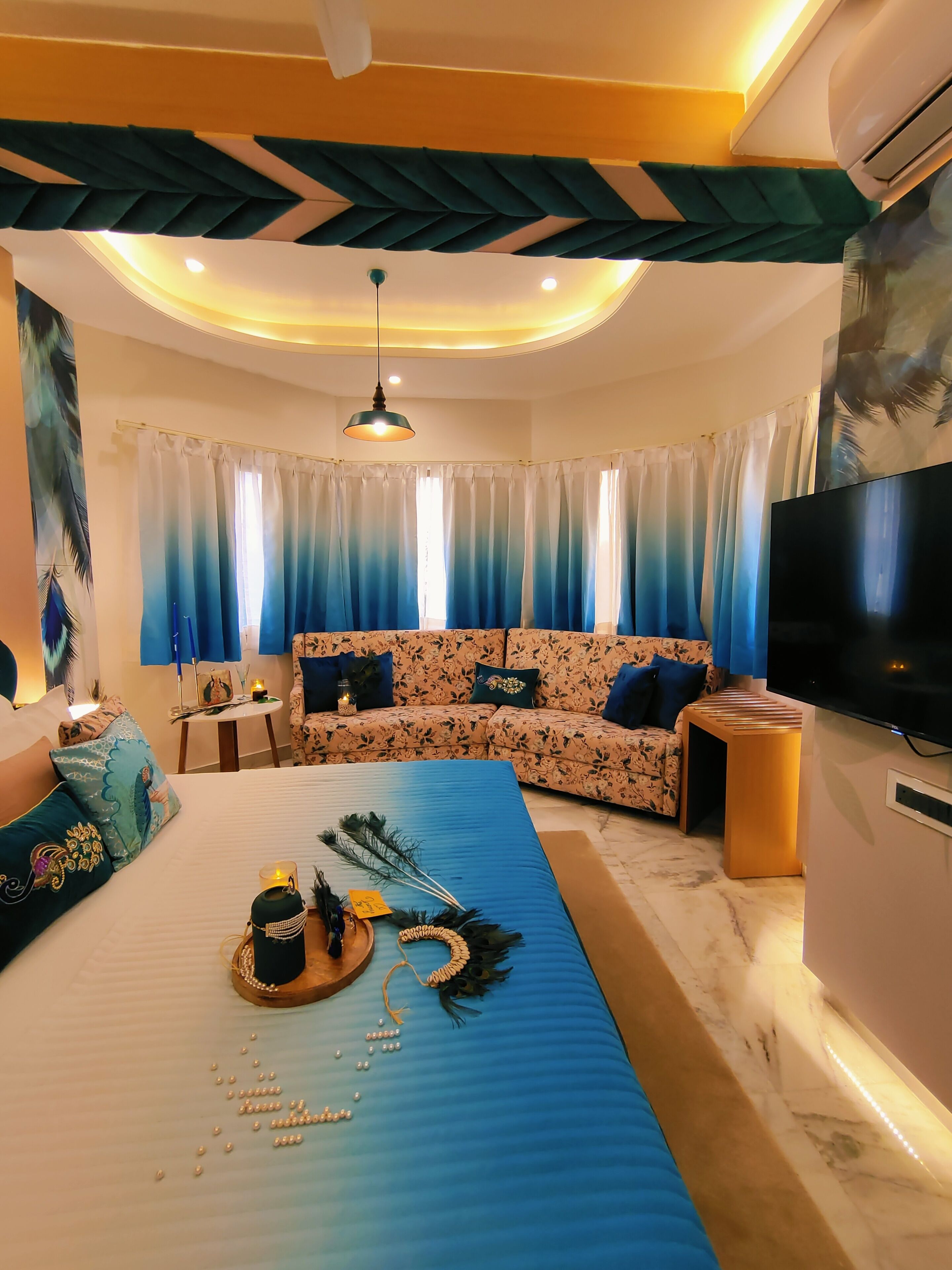 Een moderne woonkamer met een bank, een salontafel met decoratieve objecten, een televisie en een plafond met een uniek ontwerp.