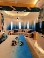 Uma sala de estar moderna com um sofá, uma mesa de centro com objetos decorativos, uma TV e um teto com design exclusivo.