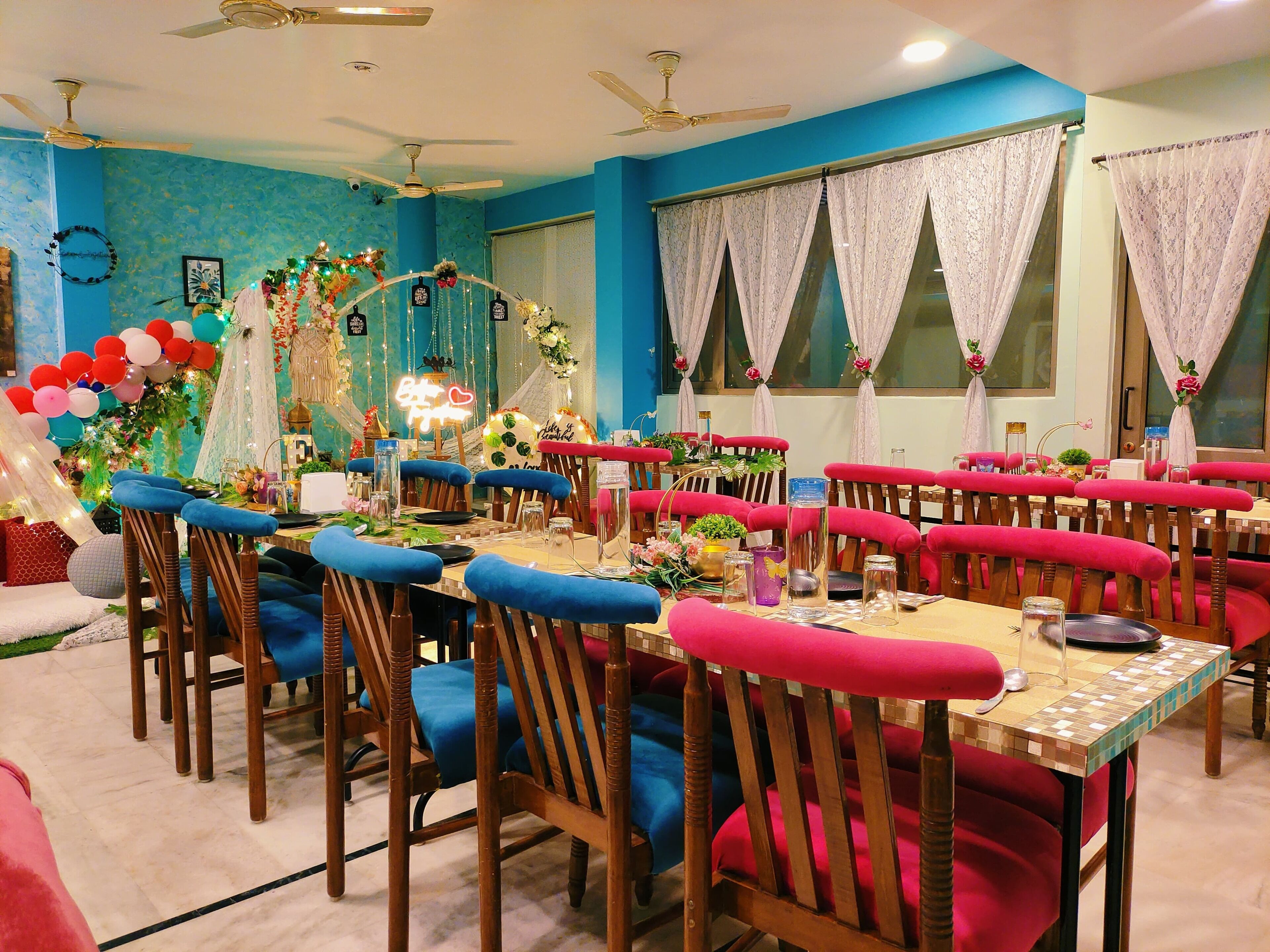 A dining area with blue and red upholstered chairs, a tiled table, and ceiling fans.