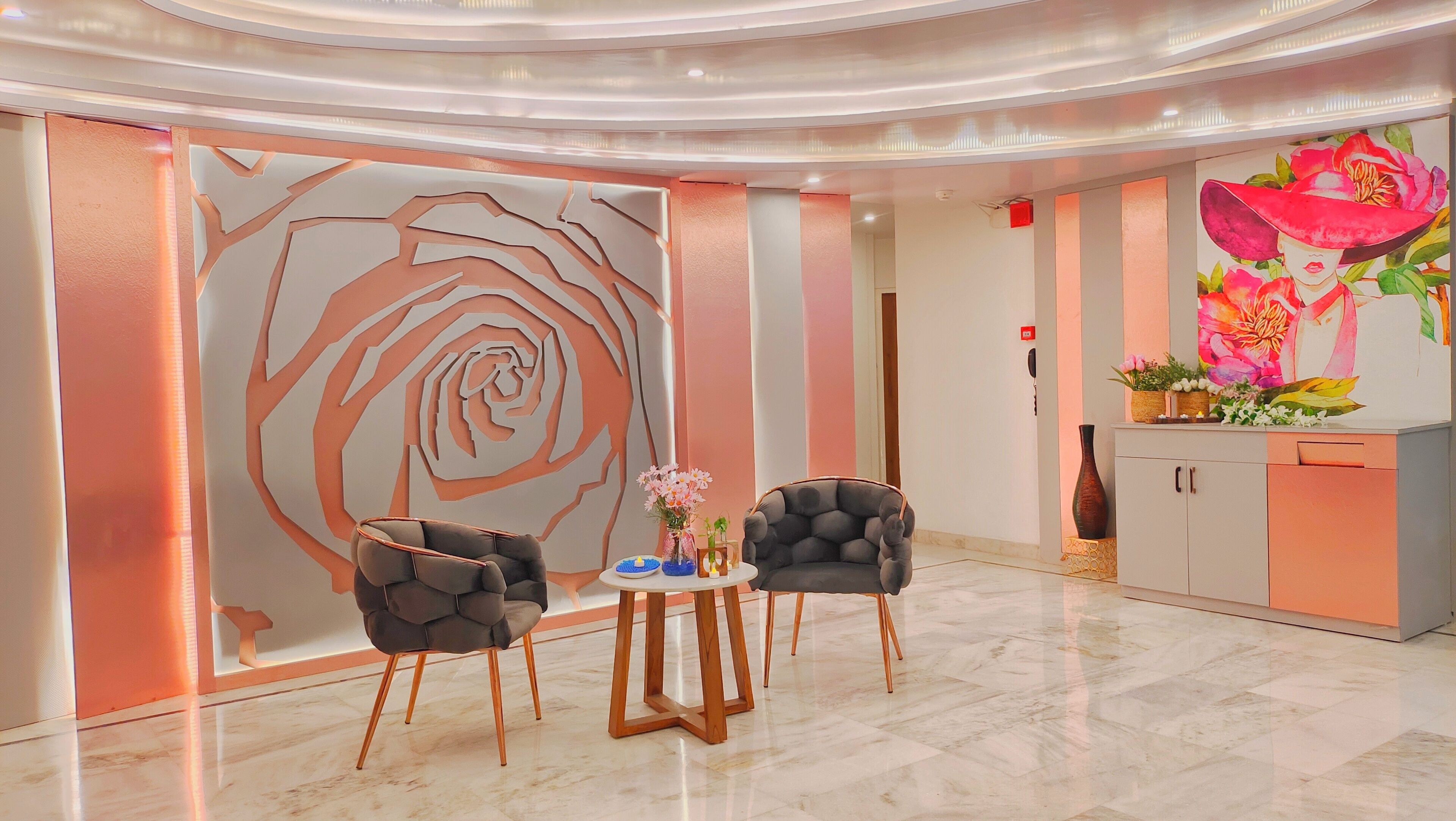 A modern lobby with a large abstract rose mural, two upholstered chairs, a small round table, and a cabinet with decorative items.