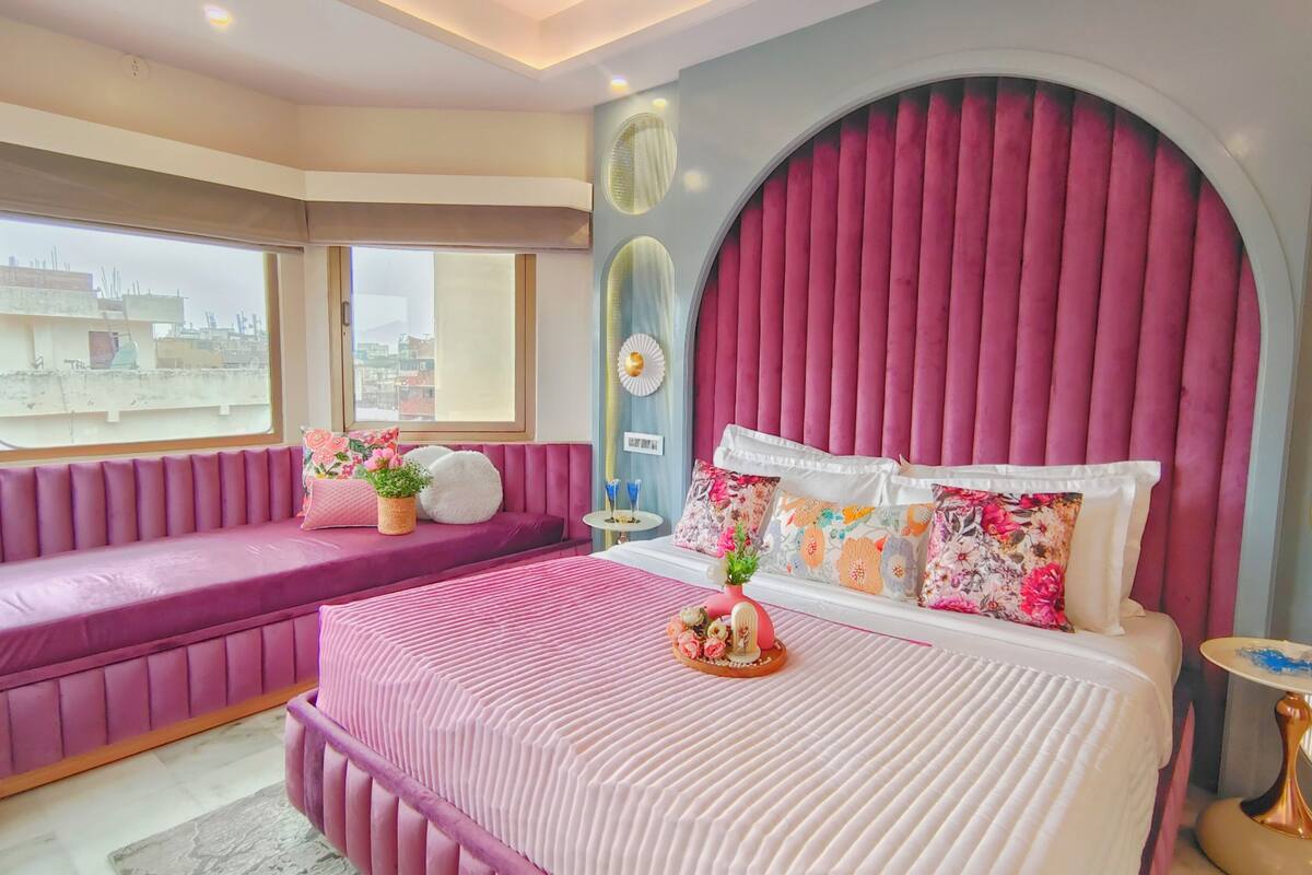 Une chambre avec un grand lit, une banquette intégrée et une fenêtre donnant sur la ville.