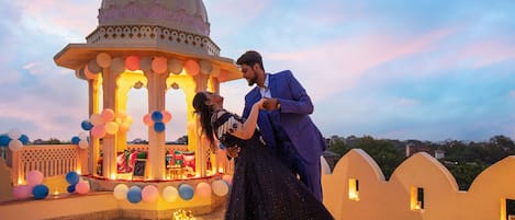 Una pareja se abraza bajo un quiosco decorativo con cúpula, rodeada de globos y luces.