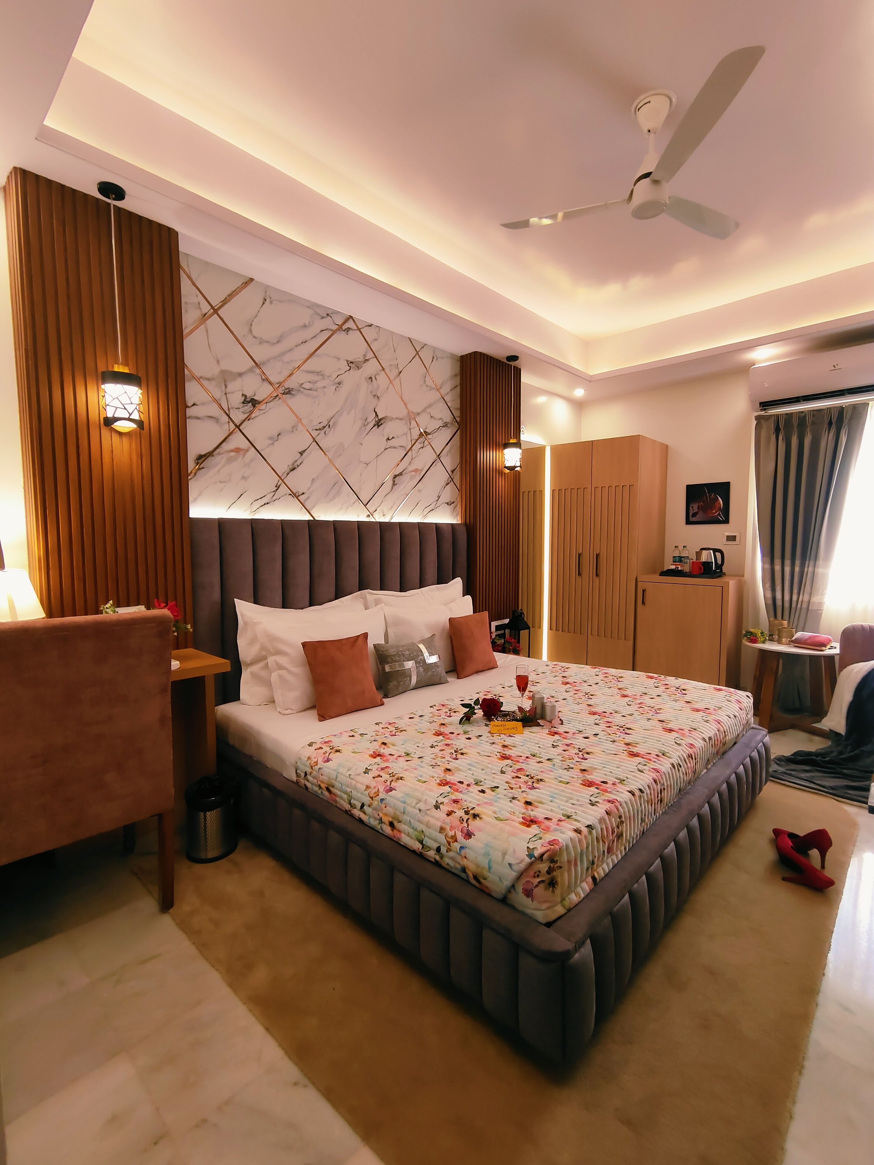 A modern bedroom with a large bed, a ceiling fan, and a marble-patterned wall.
