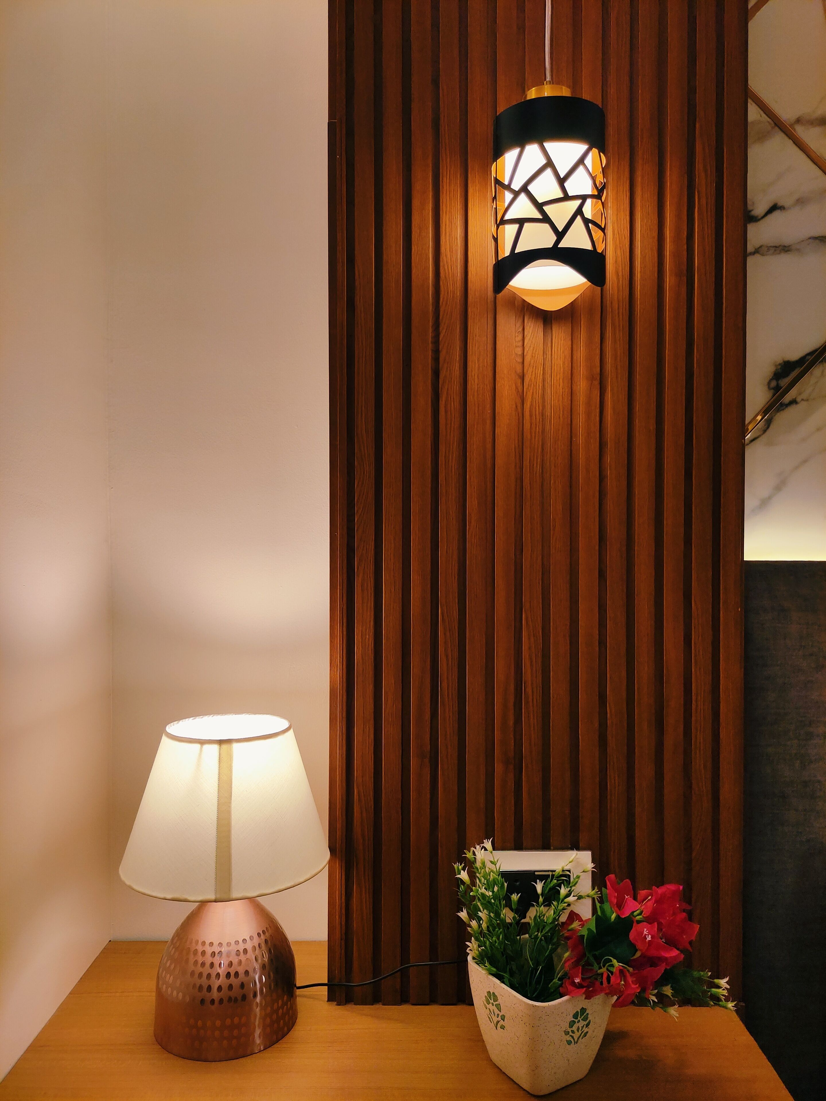 A wooden panel wall, a table lamp, and a potted plant with flowers.