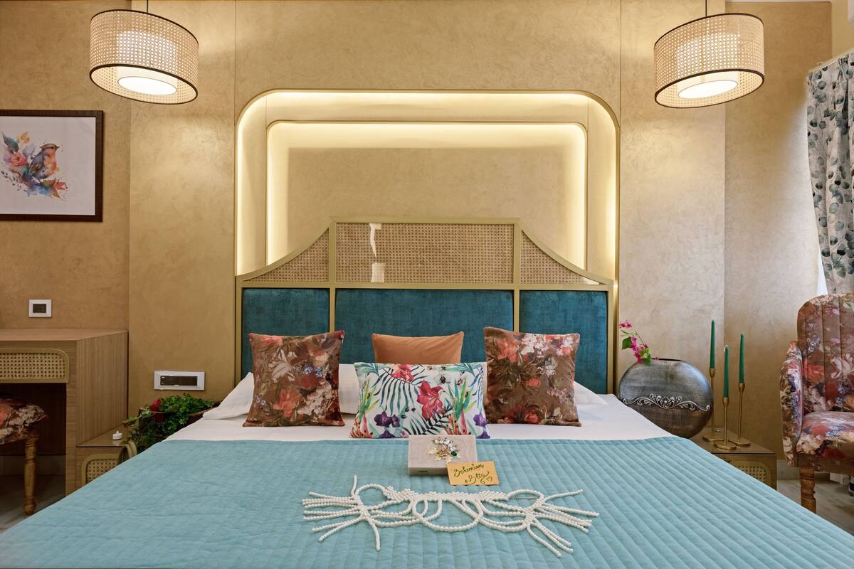 Une chambre à coucher avec un lit, des coussins à motifs floraux, une table de chevet, une lampe et une chaise.