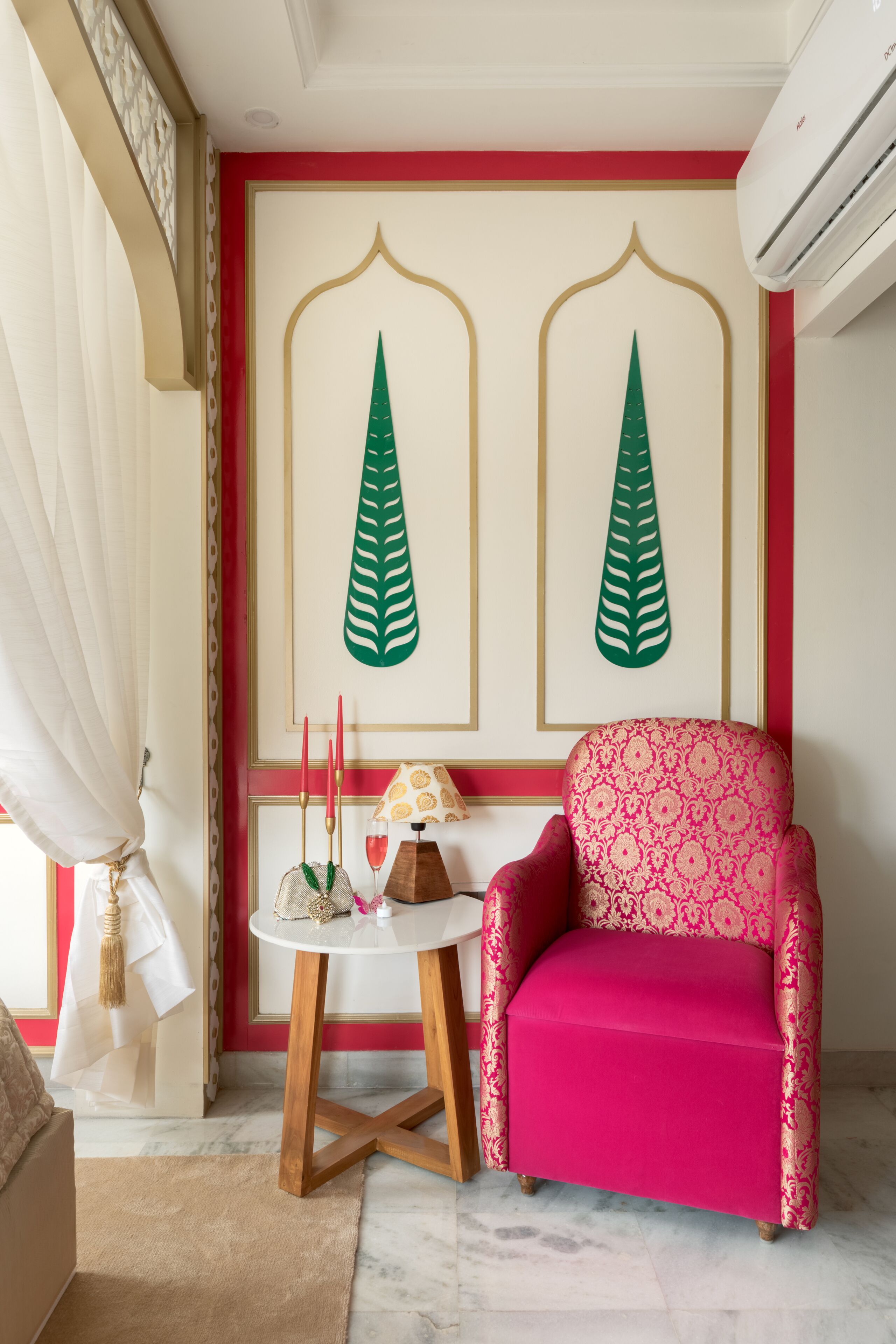 Una habitación con una decoración en rojo y blanco, un sillón estampado en rosa, una pequeña mesa redonda con una lámpara y dos paneles decorativos en la pared.