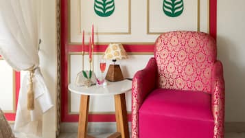 Una habitación con una decoración en rojo y blanco, un sillón estampado en rosa, una pequeña mesa redonda con una lámpara y dos paneles decorativos en la pared.