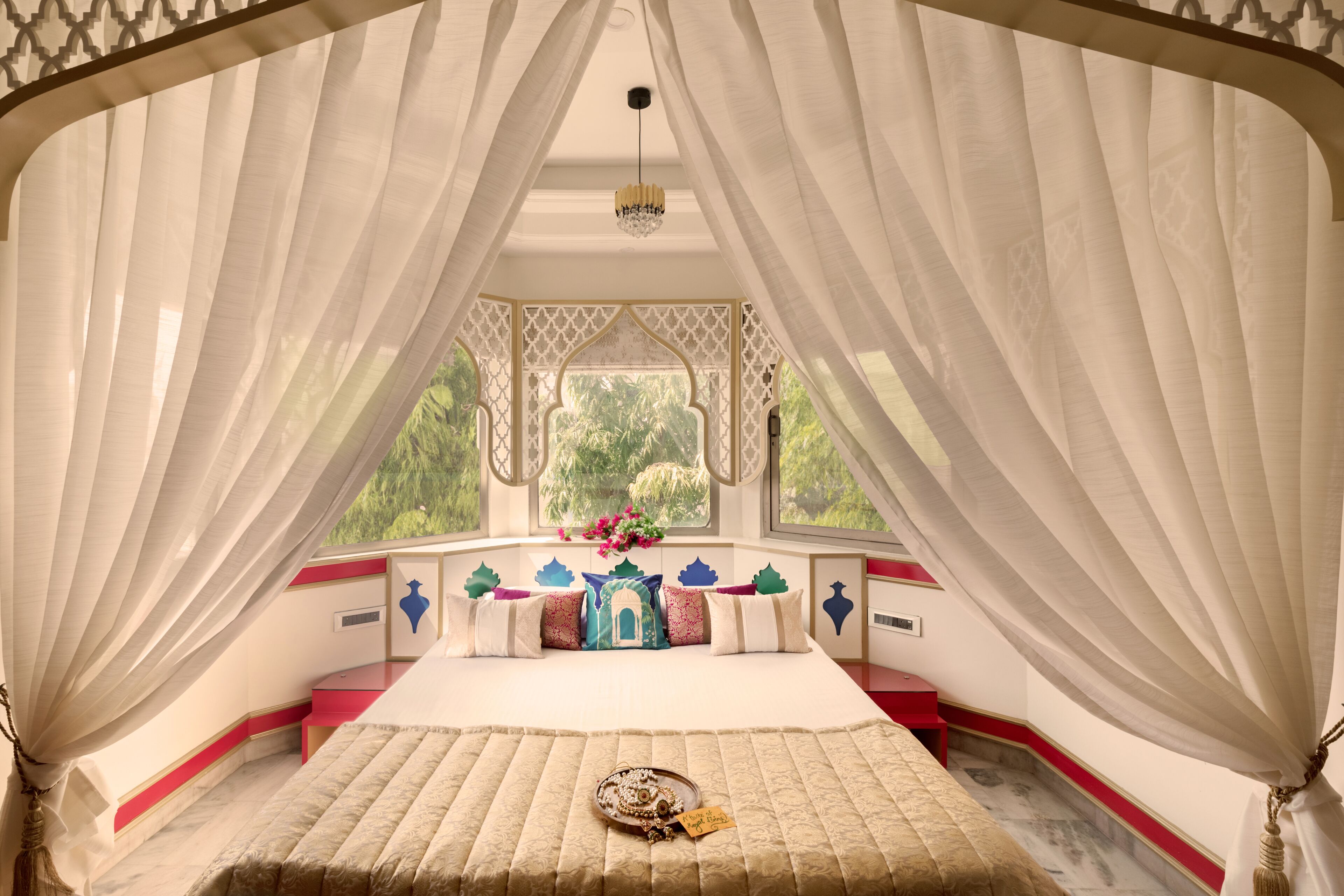 Una habitación con cama, ventana y vista a follaje decorativo.