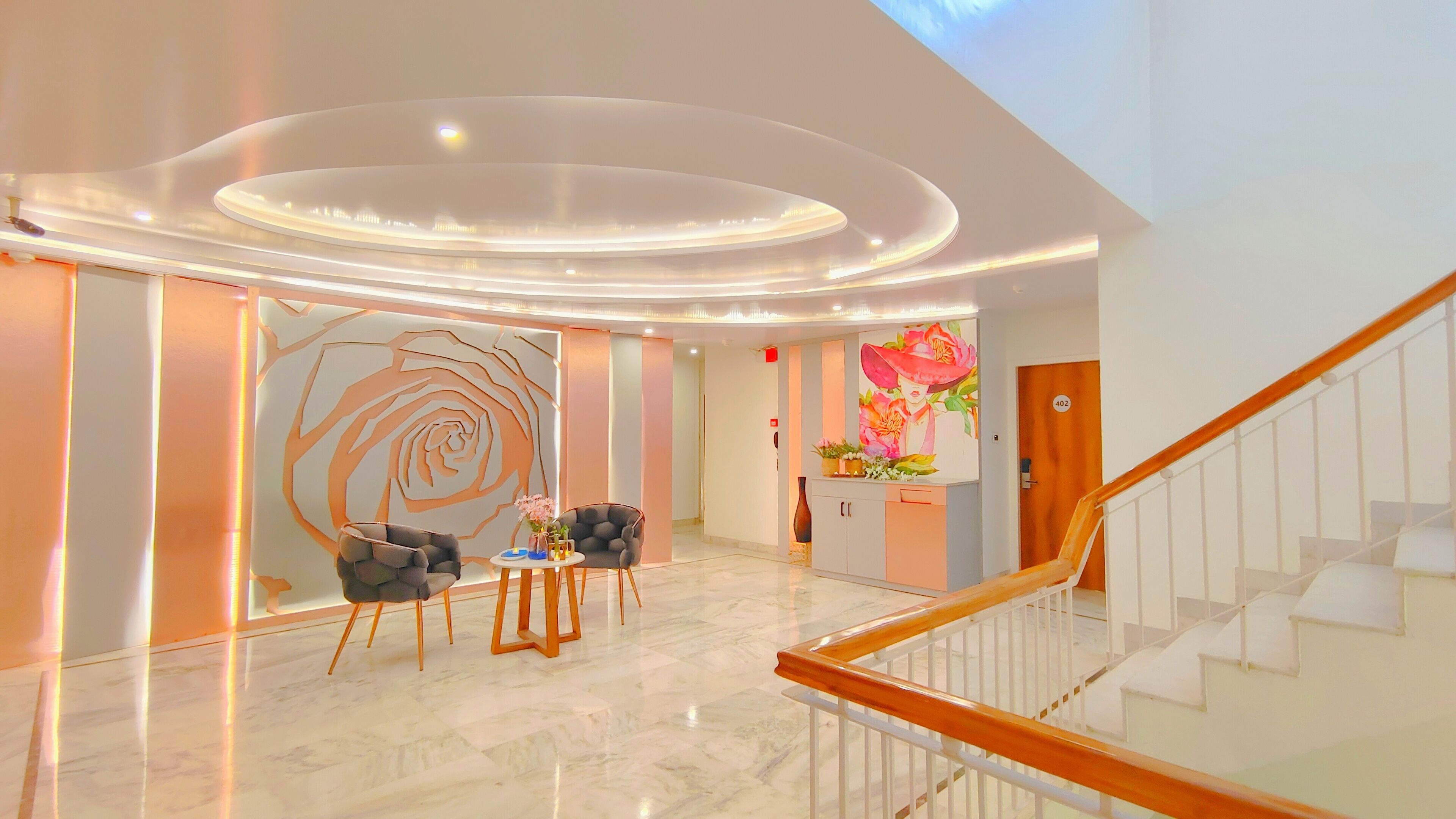 Un hall d’entrée moderne avec un sol en marbre, un escalier et un comptoir d’accueil orné d’une fresque florale.