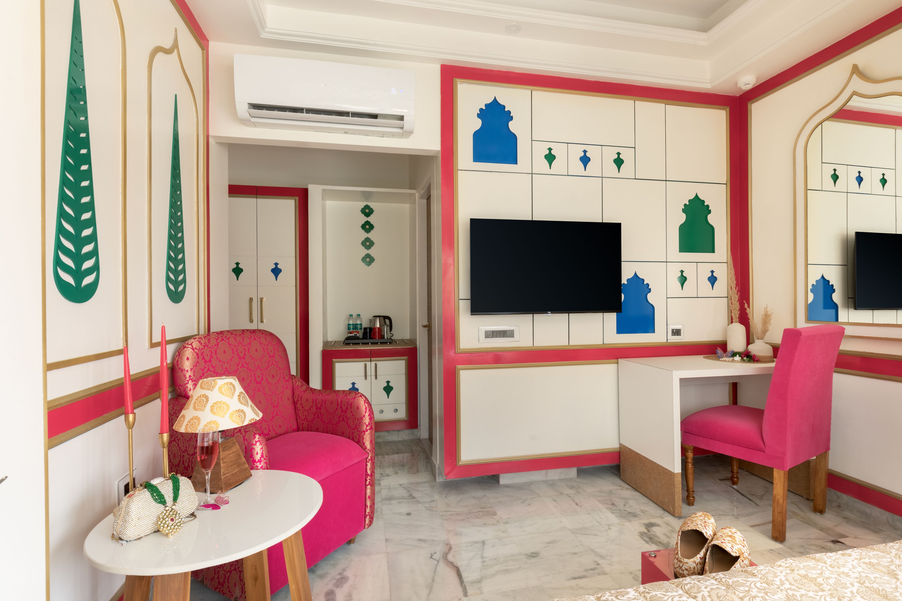 Una habitación con un sofá rosa, una mesita con una lámpara, un televisor en la pared y un escritorio con una silla.