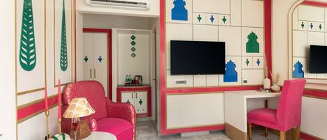 Una habitación con un sofá rosa, una mesita con una lámpara, un televisor en la pared y un escritorio con una silla.