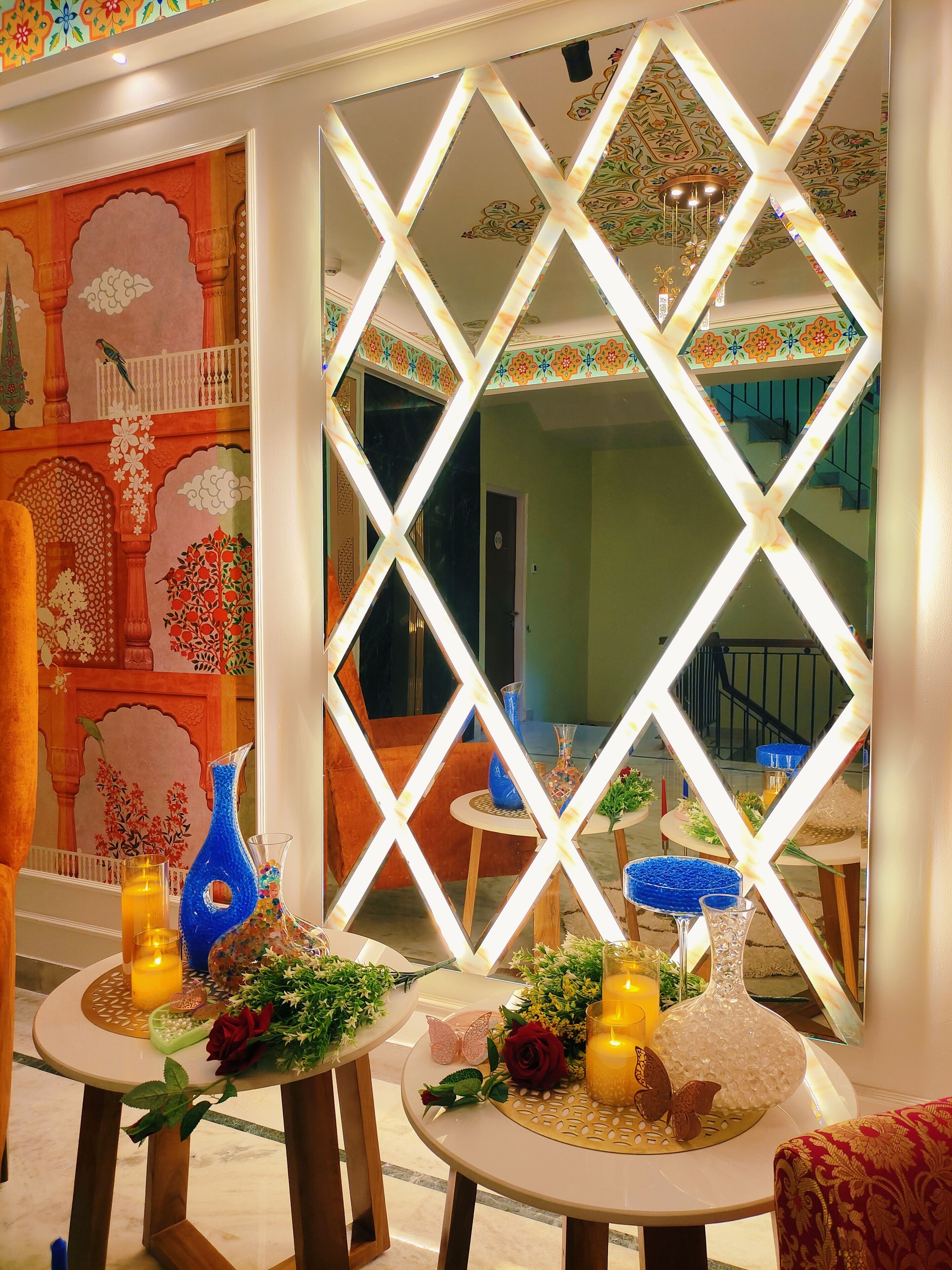 Una habitación con un separador decorativo, mesas con velas y flores, y vista a una escalera.
