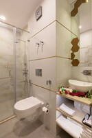 Um banheiro moderno com box de vidro, vaso sanitário branco, pia com espelho e prateleira com toalhas e produtos de higiene pessoal.