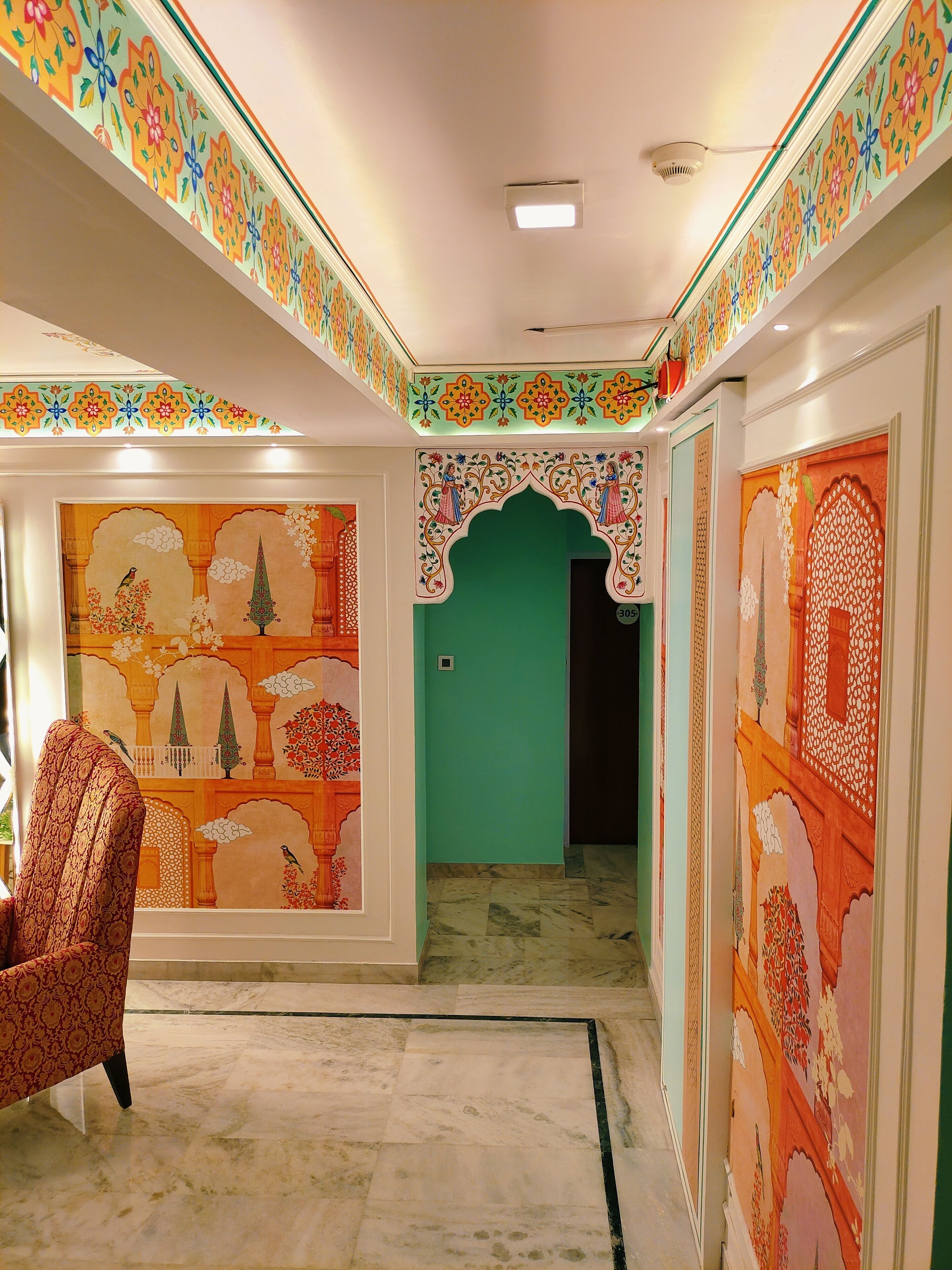 A hallway with traditional Indian wall art, a patterned armchair, and a green door.