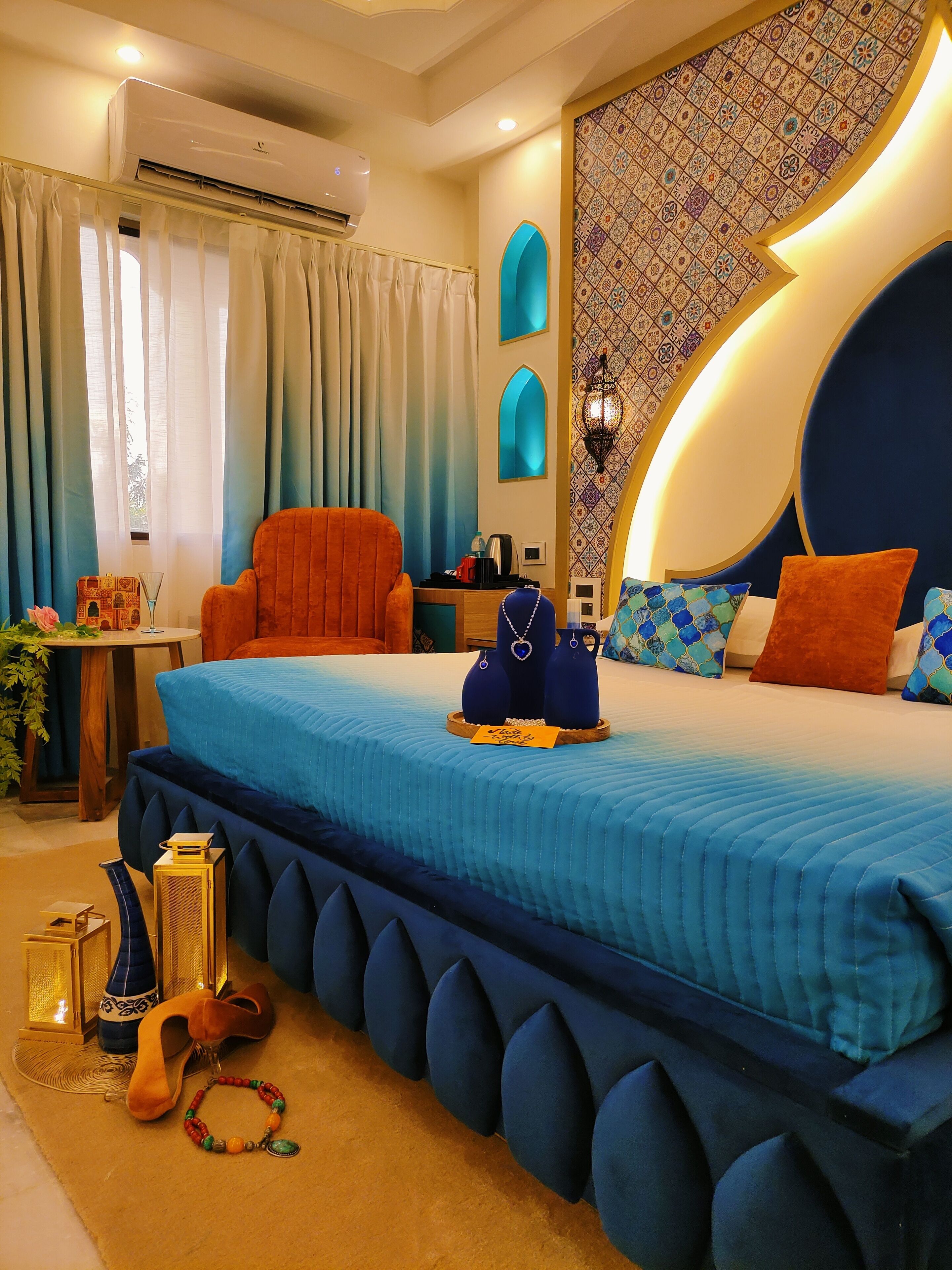 A bedroom with a large bed, a chair, an air conditioning unit, a table with a plant, and a decorative wall.